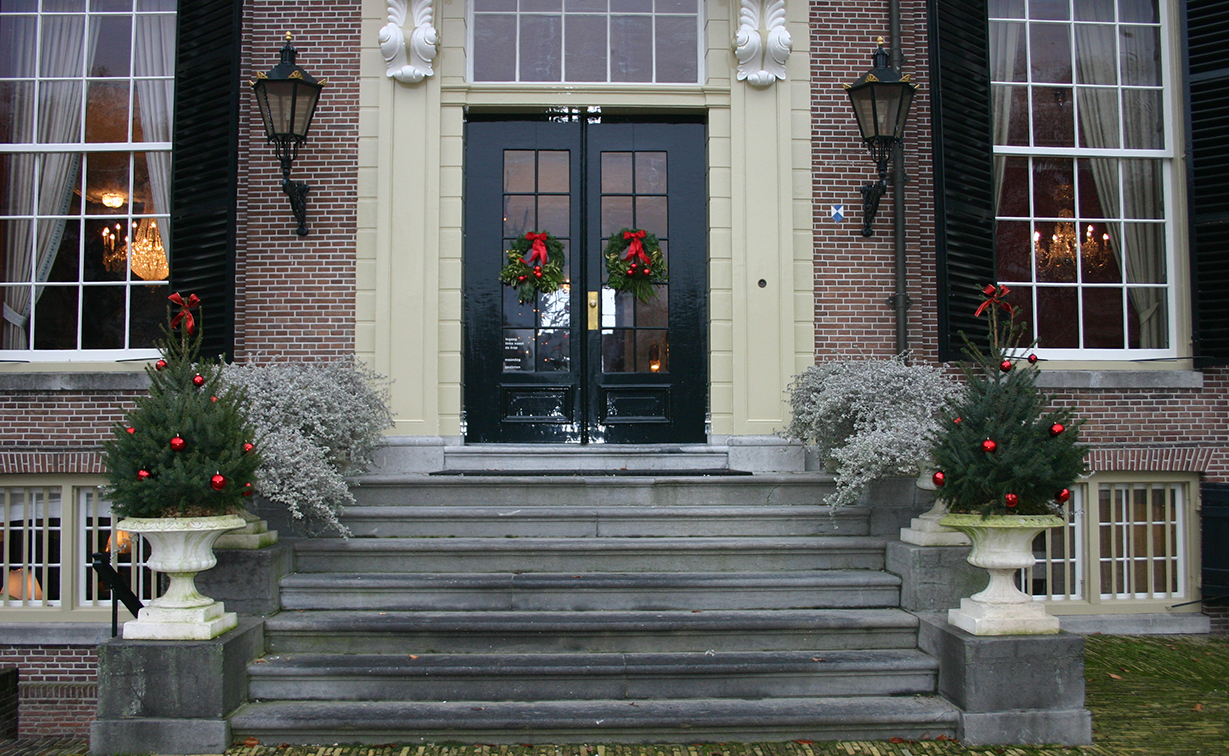 Kerst in Kasteel Groeneveld Voordeur versierd met kerststukken en kerstboompjes op de trappen